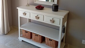 A white console table with a mirror, a bird sculpture, a bowl of cherries, and wicker baskets.