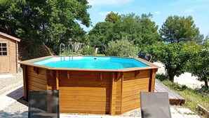 A wooden hot tub with two lounge chairs and a table with drinks, surrounded by gravel and trees.