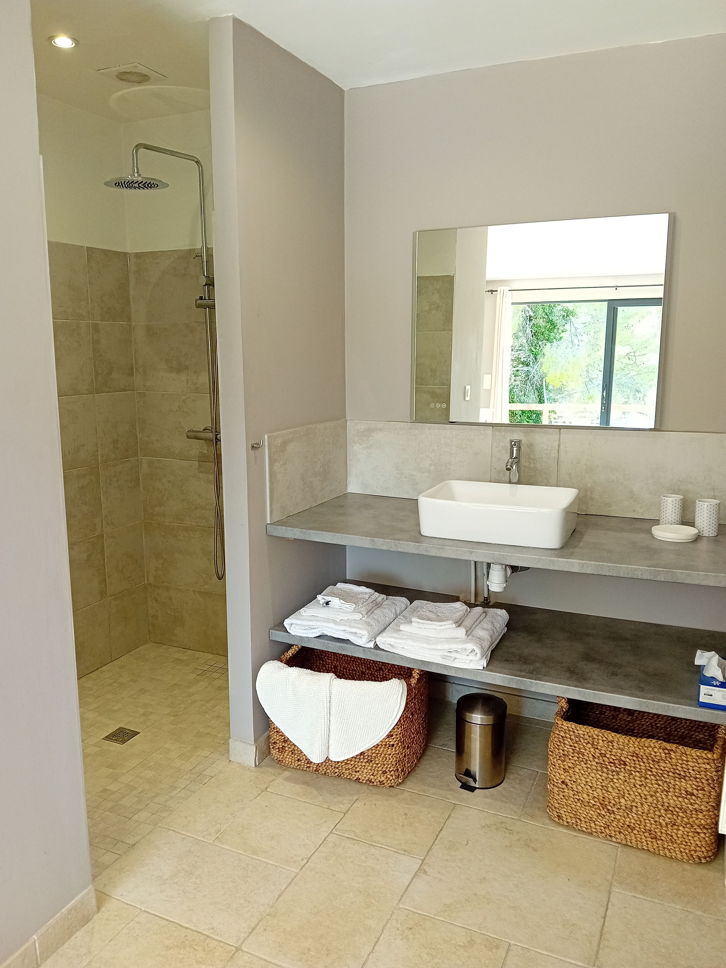 Une salle de bain moderne avec une douche, un lavabo et un miroir. On y trouve des serviettes et des paniers sous le lavabo.