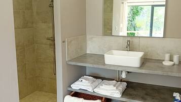Une salle de bain moderne avec une douche, un lavabo et un miroir. On y trouve des serviettes et des paniers sous le lavabo.