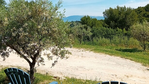 Two outdoor chairs and a small table with drinks, set on a grassy area with a tree and a view of distant hills.