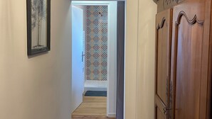 Een hal met houten vloer, een lijstwerkfoto aan de linkerkant, een behangetapijt en een houten deur aan de rechterkant.