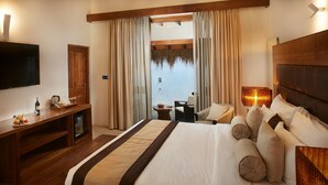 A hotel room with a large bed, wooden headboard, a TV, a desk with a coffee maker, and a view of the sea through the window. - Paradise Trinco Beach  (TRINCOMALEE SRILANKA)