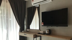 A modern hotel room with a flat-screen TV mounted on the wall, a wooden desk with a telephone and two mugs, and a coffee maker.
