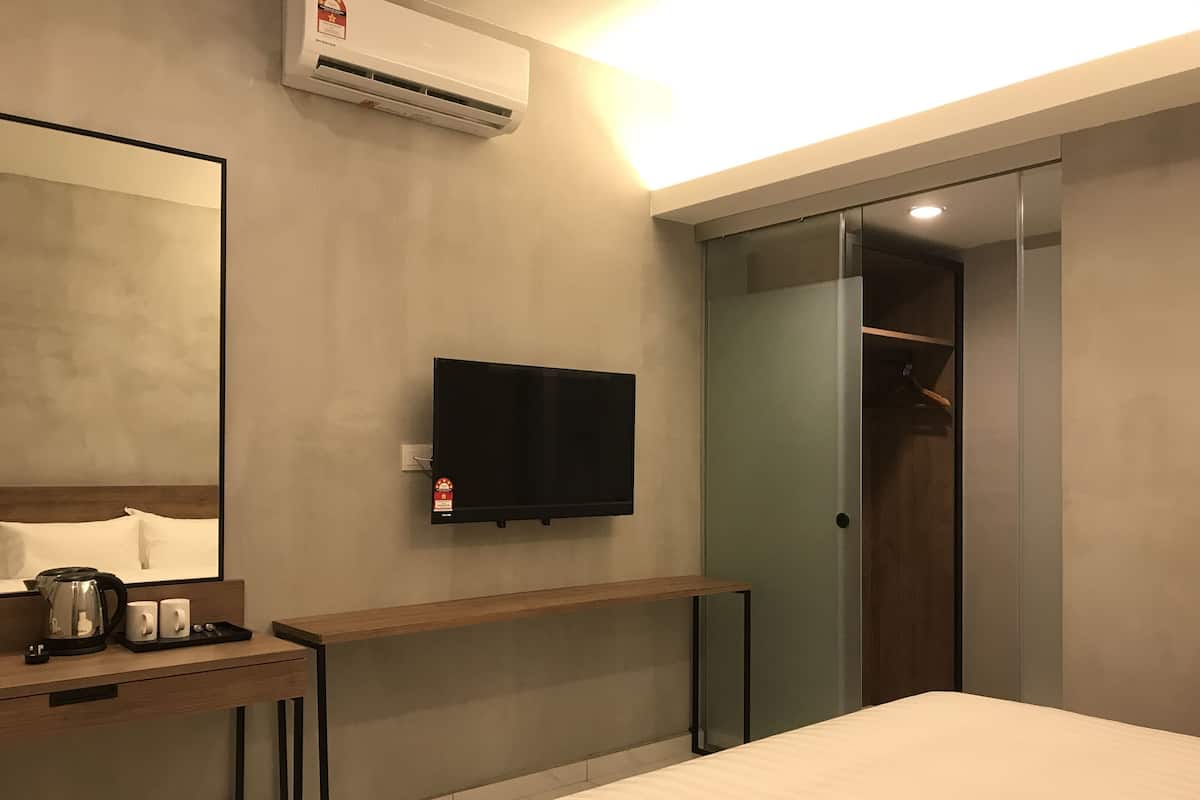 Habitación de hotel con cama, mesita de noche con tetera y tazas, televisor de pantalla plana y puerta corredera al armario.