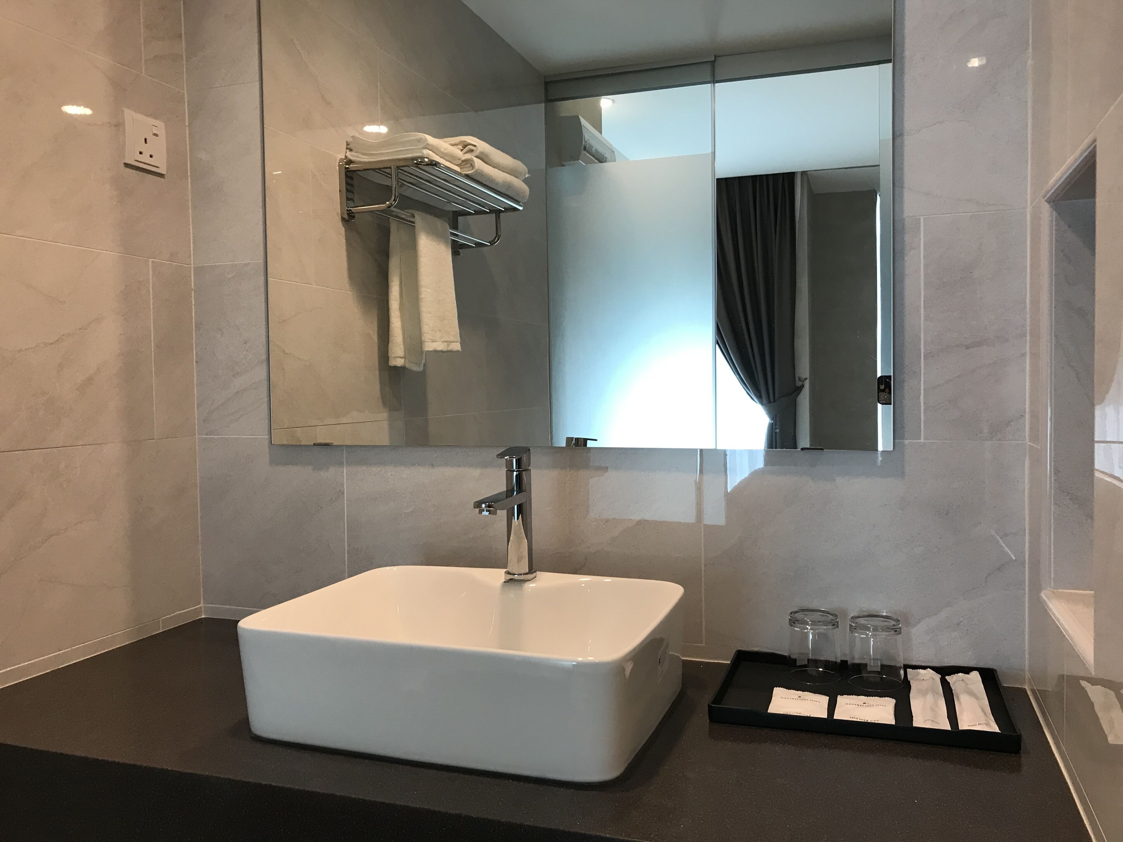 A modern bathroom with a large white sink, a towel rack, a mirror, and a tray with toiletries.