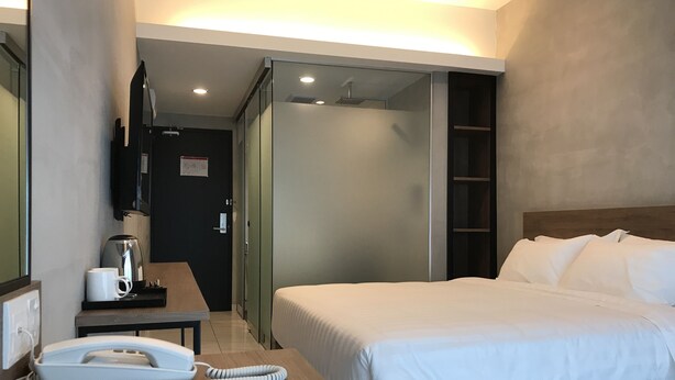 A hotel room with a bed, a desk with a telephone, a coffee maker, and a TV mounted on the wall.