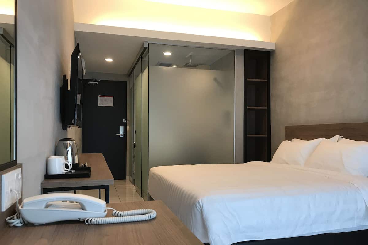 Habitación de hotel con cama, escritorio con teléfono, cafetera y televisor montado en la pared.