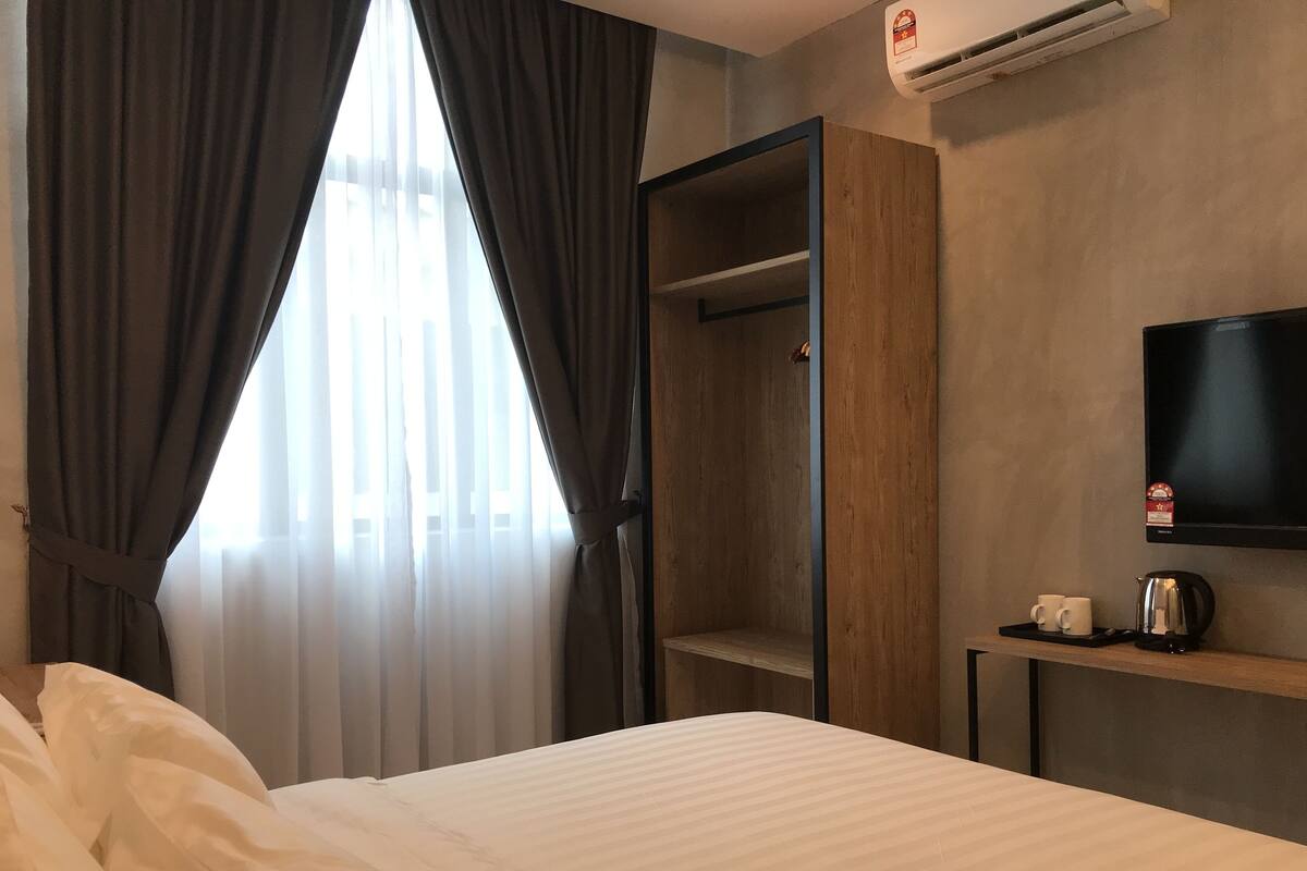 Una habitación de hotel con una cama, un armario, un televisor y una cafetera.