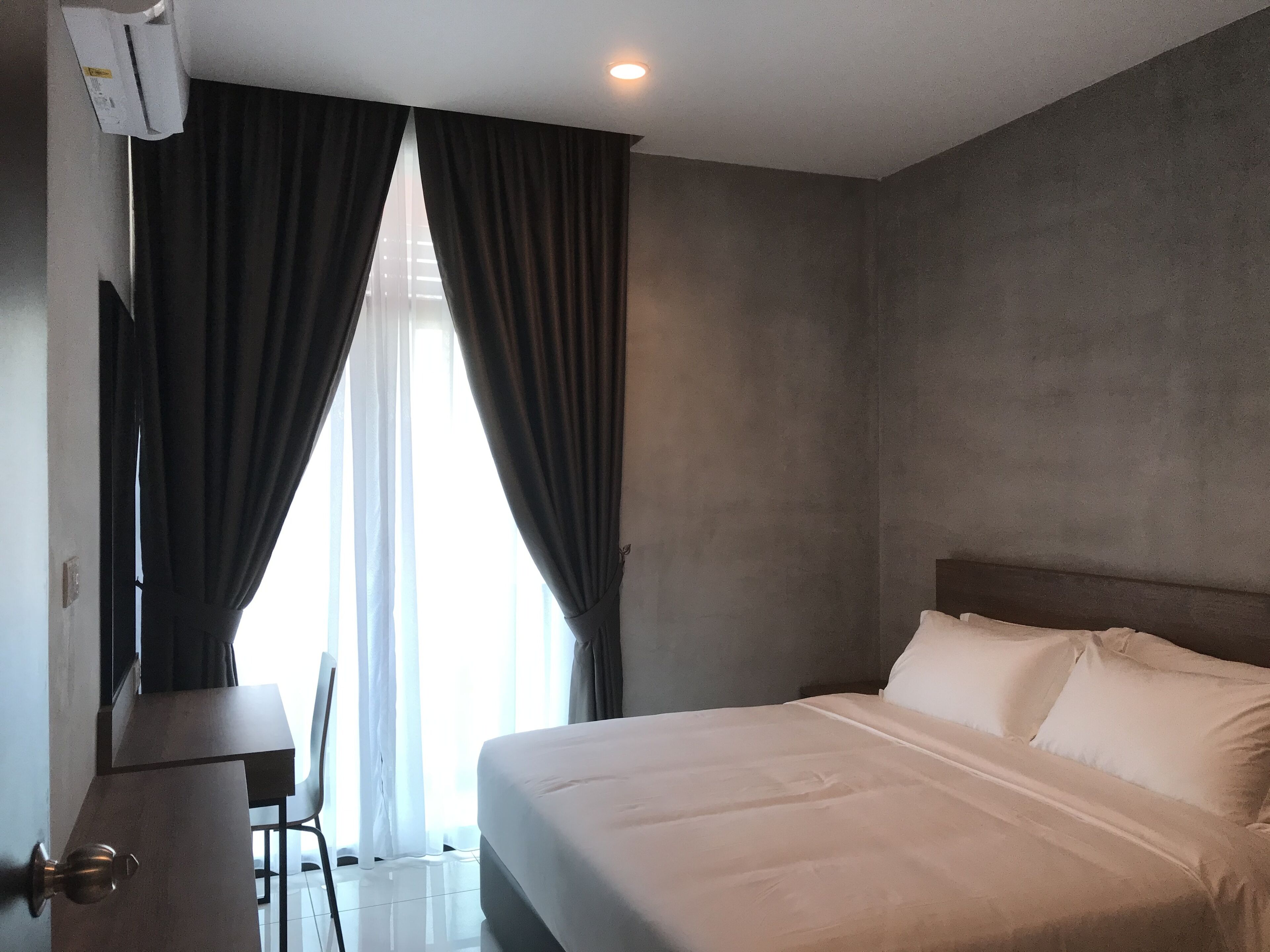 A hotel room with a bed, curtains, a chair, and a TV.
