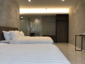 A modern hotel room with two beds, a wooden headboard, a small table, and a wardrobe.