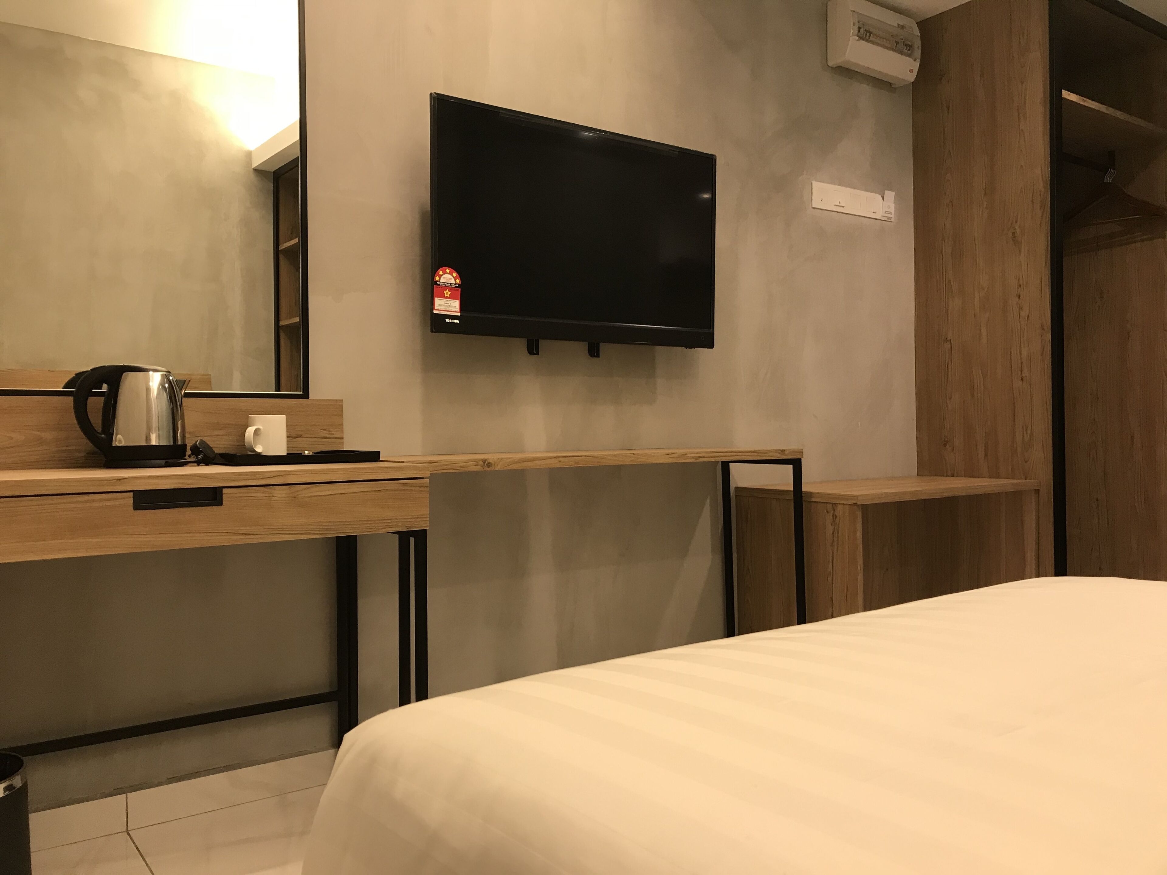 A hotel room with a bed, a desk with a kettle, a flat-screen TV, and a wooden wardrobe.