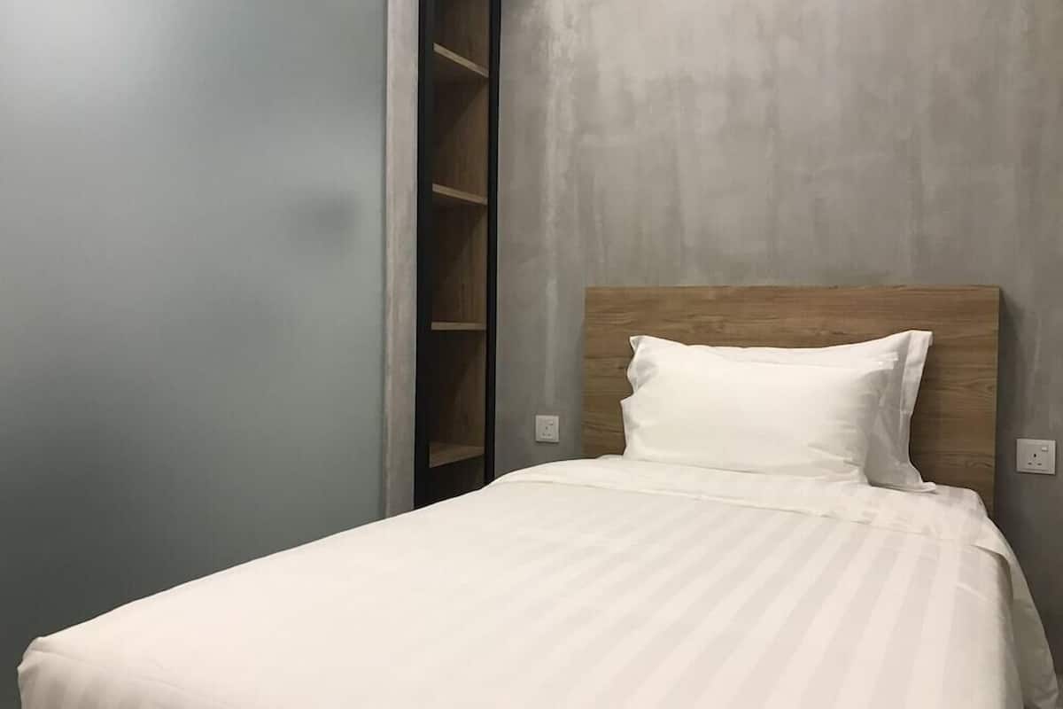 Una cama con cabecera de madera, almohada blanca y pared gris.