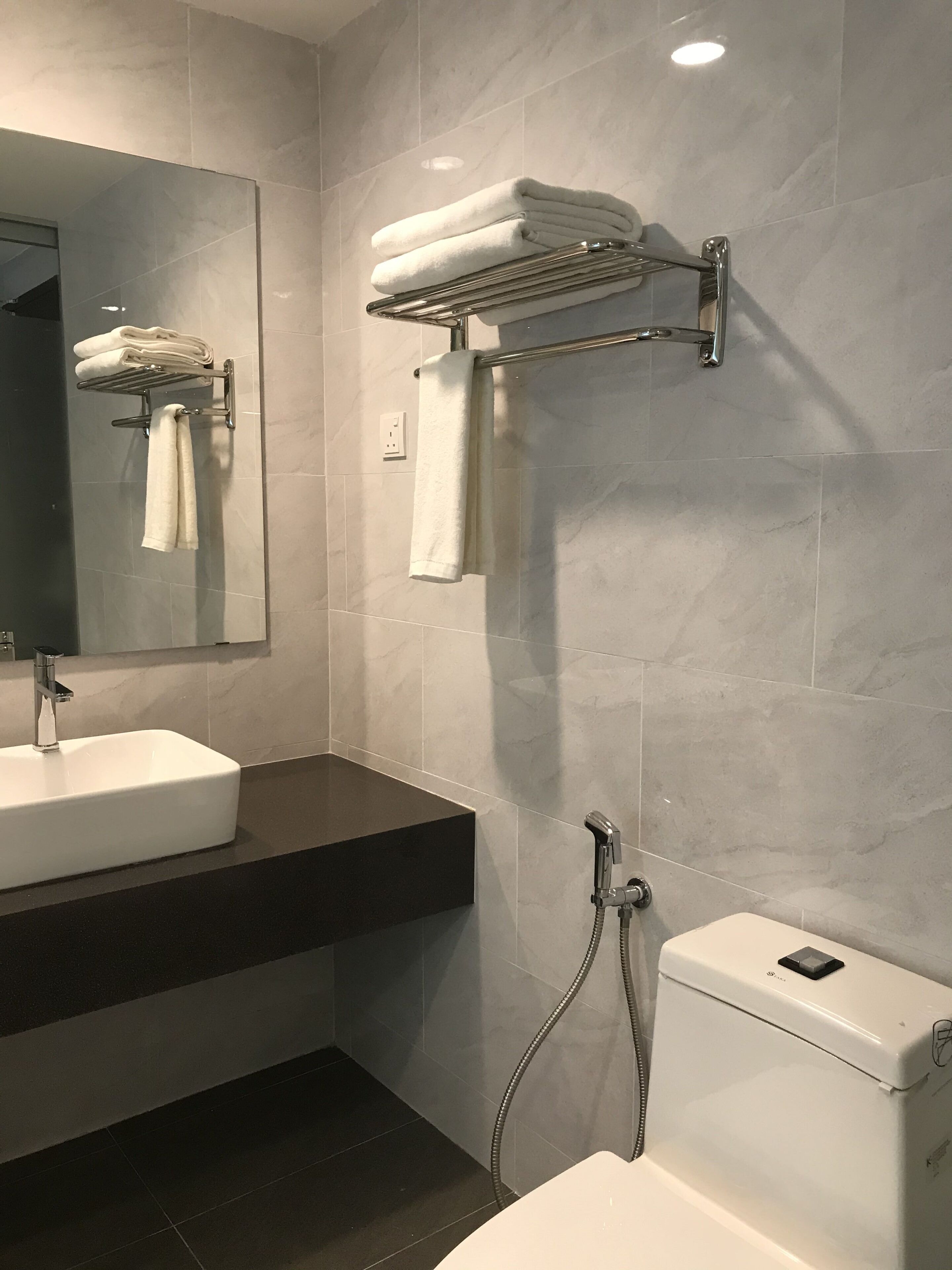 A modern bathroom with a white sink, a toilet, and a towel rack with folded towels.