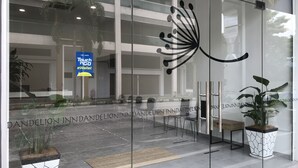 A modern building entrance with a glass door, a logo on the glass, and a sign for Touch 'n Go eWallet.