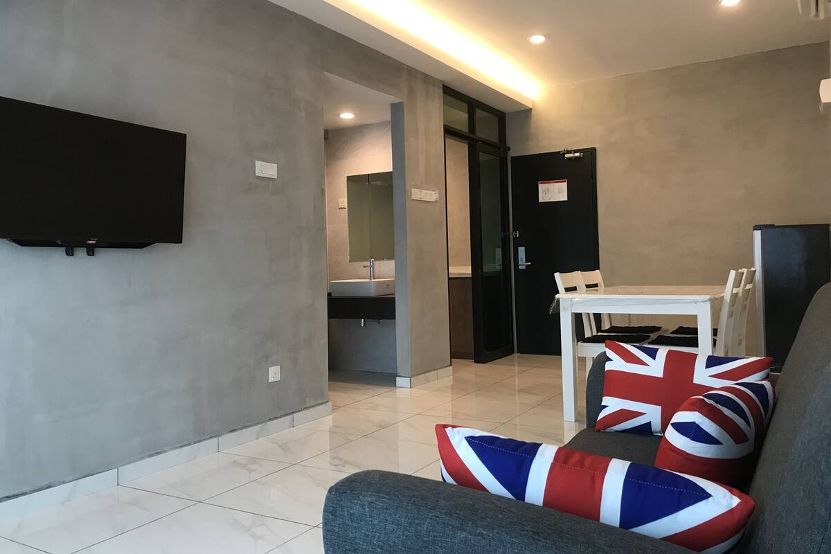 Una sala moderna con un televisor de pantalla plana, una mesa de comedor con sillas y un sofá con cojines con la bandera británica.