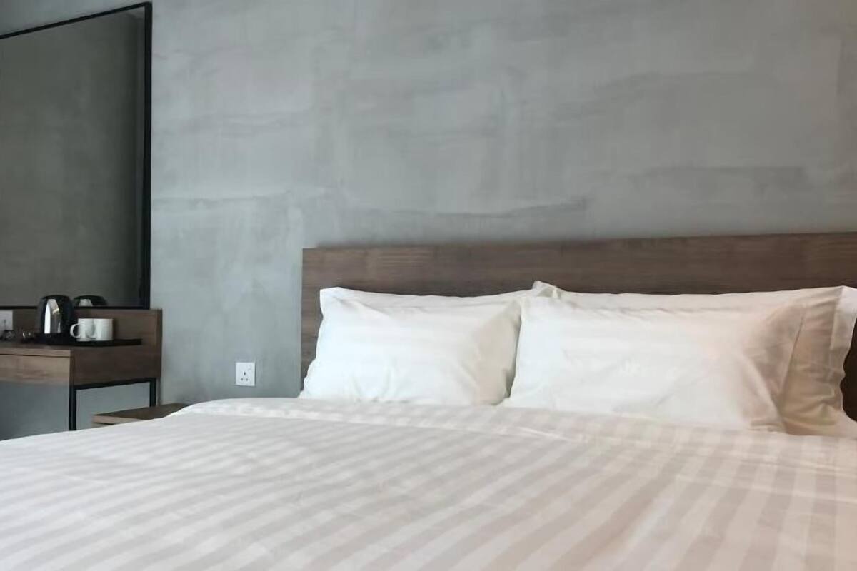 Una habitación de hotel con una cama grande, una mesita de noche de madera con un teléfono y una cafetera, y un espejo grande en la pared.