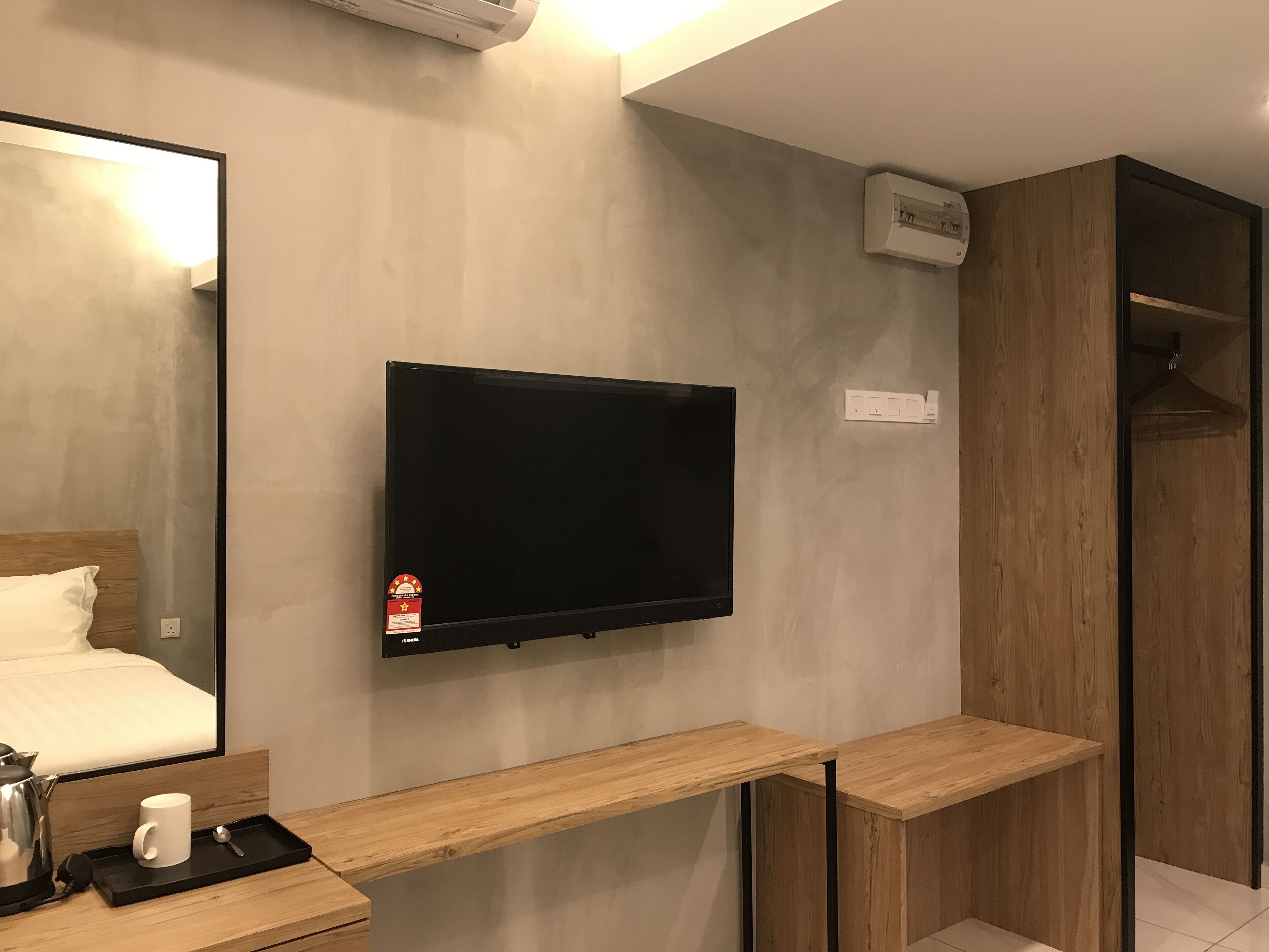Habitación de hotel moderna con televisión montada, muebles de madera, un espejo y una cama con edredón blanco.