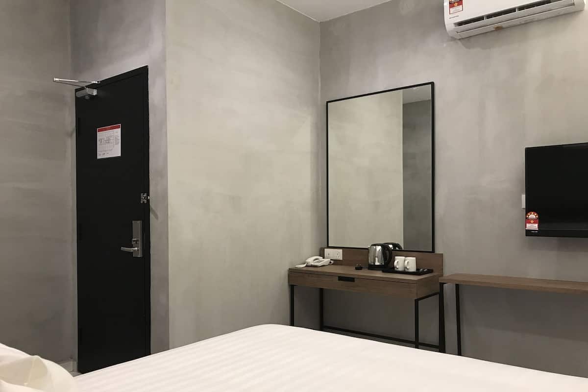 Habitación de hotel con cama, mesita de noche con teléfono y tetera, espejo, televisor montado en la pared y equipo de aire acondicionado.