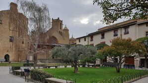 Un pati amb una banca de pedra, una zona verda i un edifici històric amb una torre campanar.