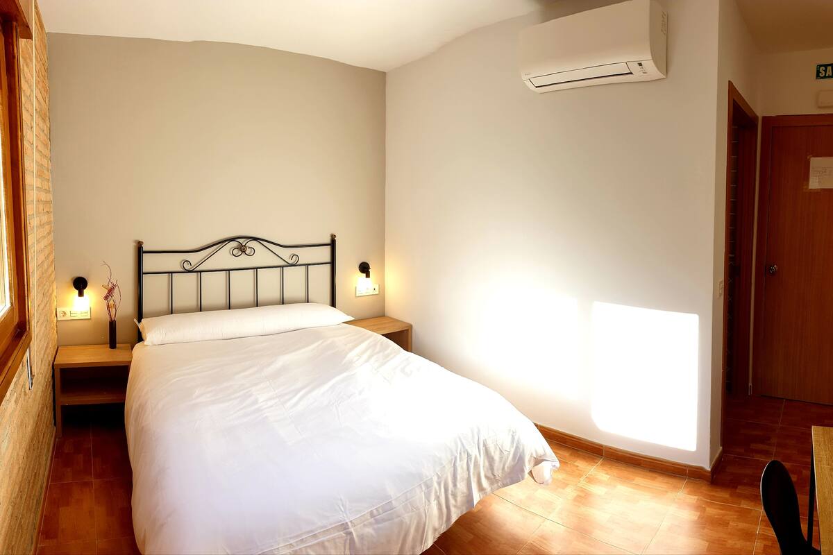 Quarto com cama, luminárias de cabeceira, ar condicionado e porta com placa.