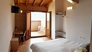 Un dormitori amb un llit, una taula de treball i una cadira. Hi ha una televisió penjada a la paret i una finestra que ofereix vistes a l'exterior.