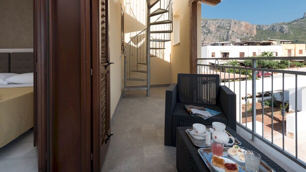 A balcony with a dining table set, a wicker chair, and a spiral staircase. - La Dimora del Pescatore (San Vito Lo Capo)