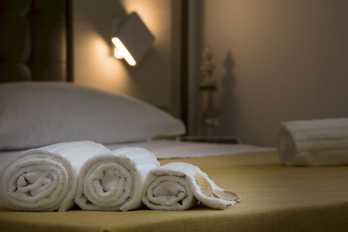 Ein ordentlich bezogenes Bett mit aufgerollten weißen Handtüchern und einer gelben Bettdecke.