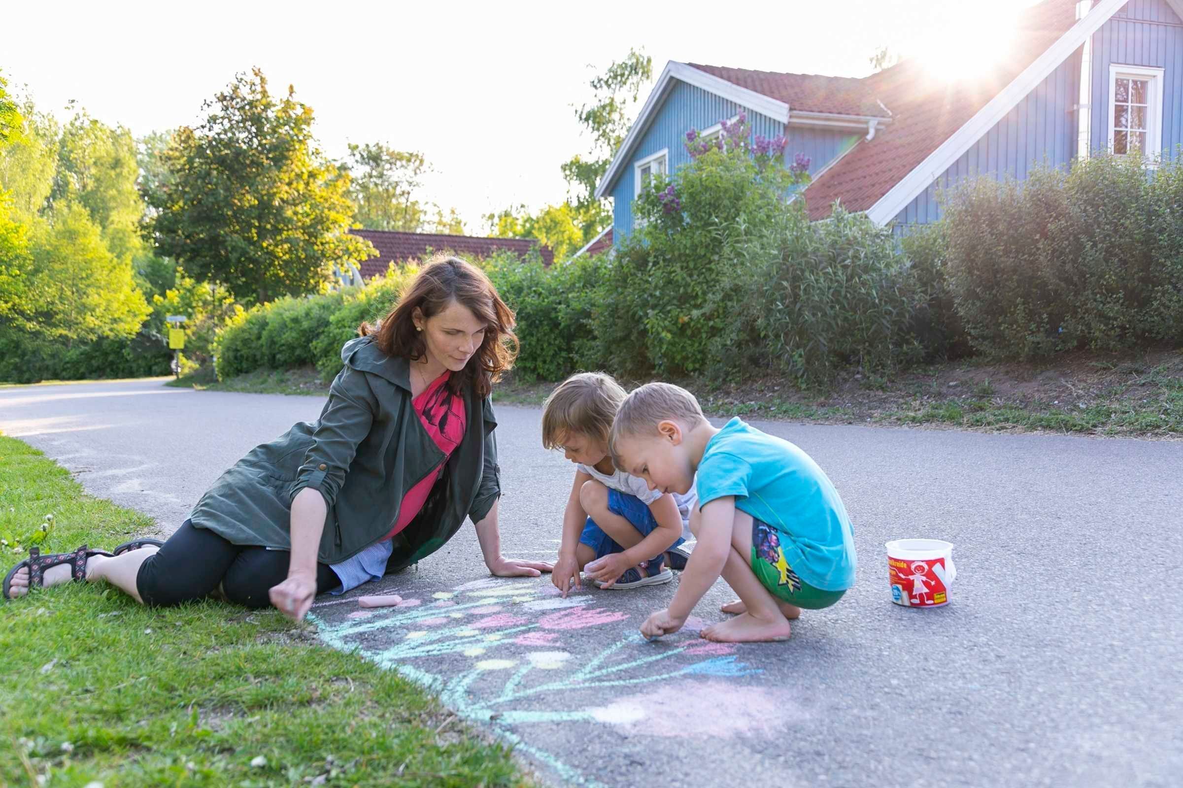 Een vrouw en twee kinderen spelen met krijt op een geplaveid oppervlak.