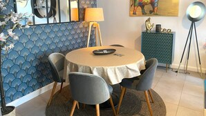 Un comedor con una mesa redonda, cuatro sillas, un espejo decorativo, una lámpara, un cuadro en la pared de un elefante y un mueble con un diseño azul turquesa.