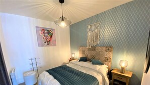Un dormitorio con cama, mesitas de noche, cabecera, un cuadro en la pared y una lámpara en el techo.
