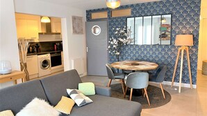 Un espacio habitable compacto con kitchenette, comedor y zona de estar con sofá y sillones.