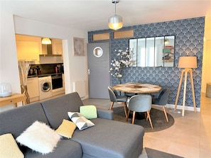 Un espacio habitable compacto con kitchenette, comedor y zona de estar con sofá y sillones.