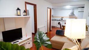 A living room with a TV, a sofa, a coffee table, and a plant. - Apartamentos Costa Norte (San Vicente de la Barquera)