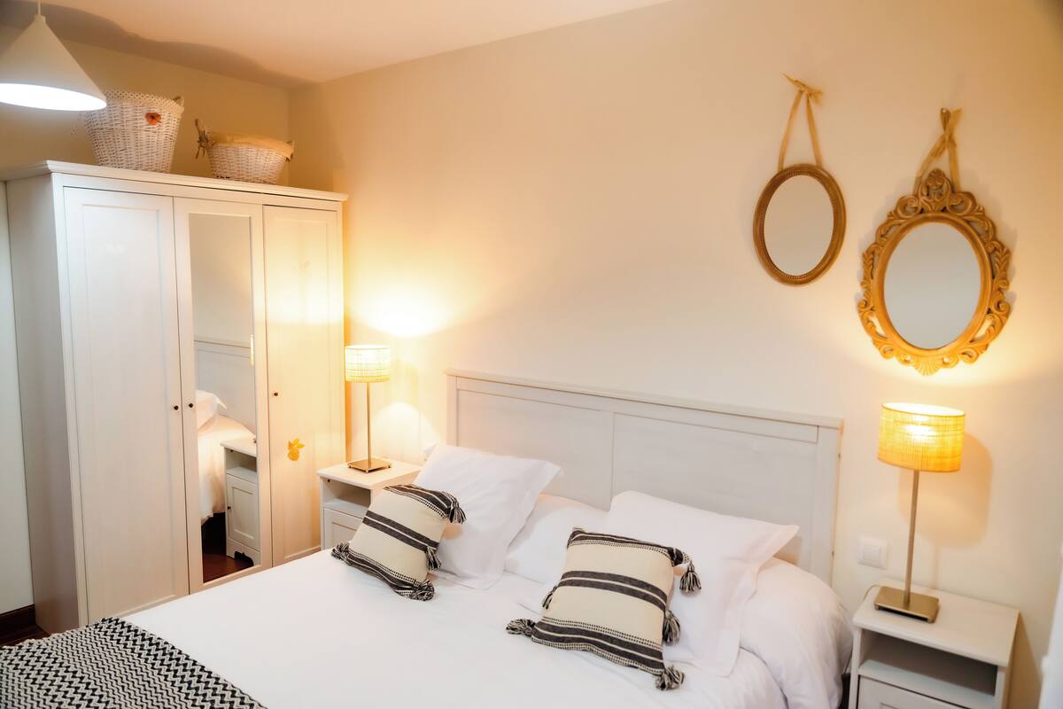 Un lit bien fait, avec du linge de lit blanc et des oreillers à rayures, une armoire blanche et deux lampes de chevet.