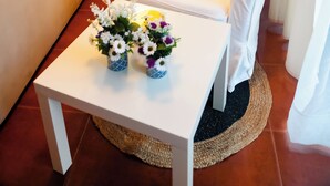 A white armchair, a white table with a vase of flowers, a beige sofa, and a floor lamp in a living room. - Apartamentos Costa Norte (San Vicente de la Barquera)