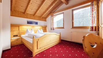 A wooden bedroom with a bed, a nightstand, a chair, and a window with a view of mountains.