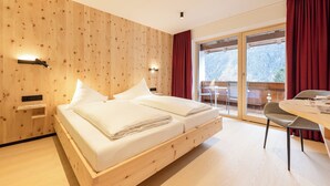 A modern bedroom with a wooden wall, a large bed, a dining table, and a view of a snowy landscape. - Gasthof Gröbenhof (Fulpmes)