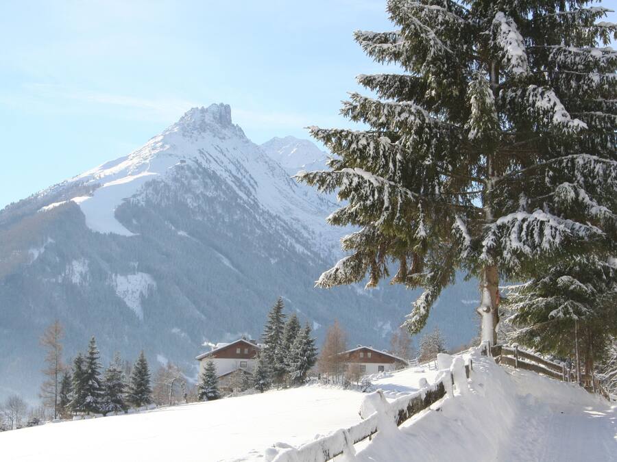 A snow-covered mountain with a chalet and a wooden fence.