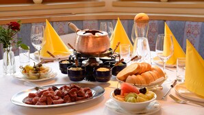 A breakfast setting with a variety of dishes, including meats, fruits, and bread, arranged on a table with yellow napkins and a copper pot. - Gasthof Gröbenhof (Fulpmes)