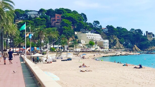 A coastal beach scene with a paved walkway, beach umbrellas, and people relaxing on the sand. - Panoramic Sea View and Private Pool (Lloret de Mar)