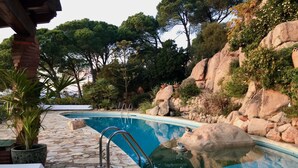 A swimming pool with stone tiles, metal ladders, and surrounding greenery. - Panoramic Sea View and Private Pool (Lloret de Mar)