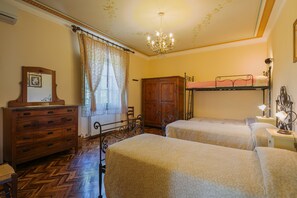 Une chambre avec deux lits, une commode en bois, un lustre et une fenêtre avec des rideaux.