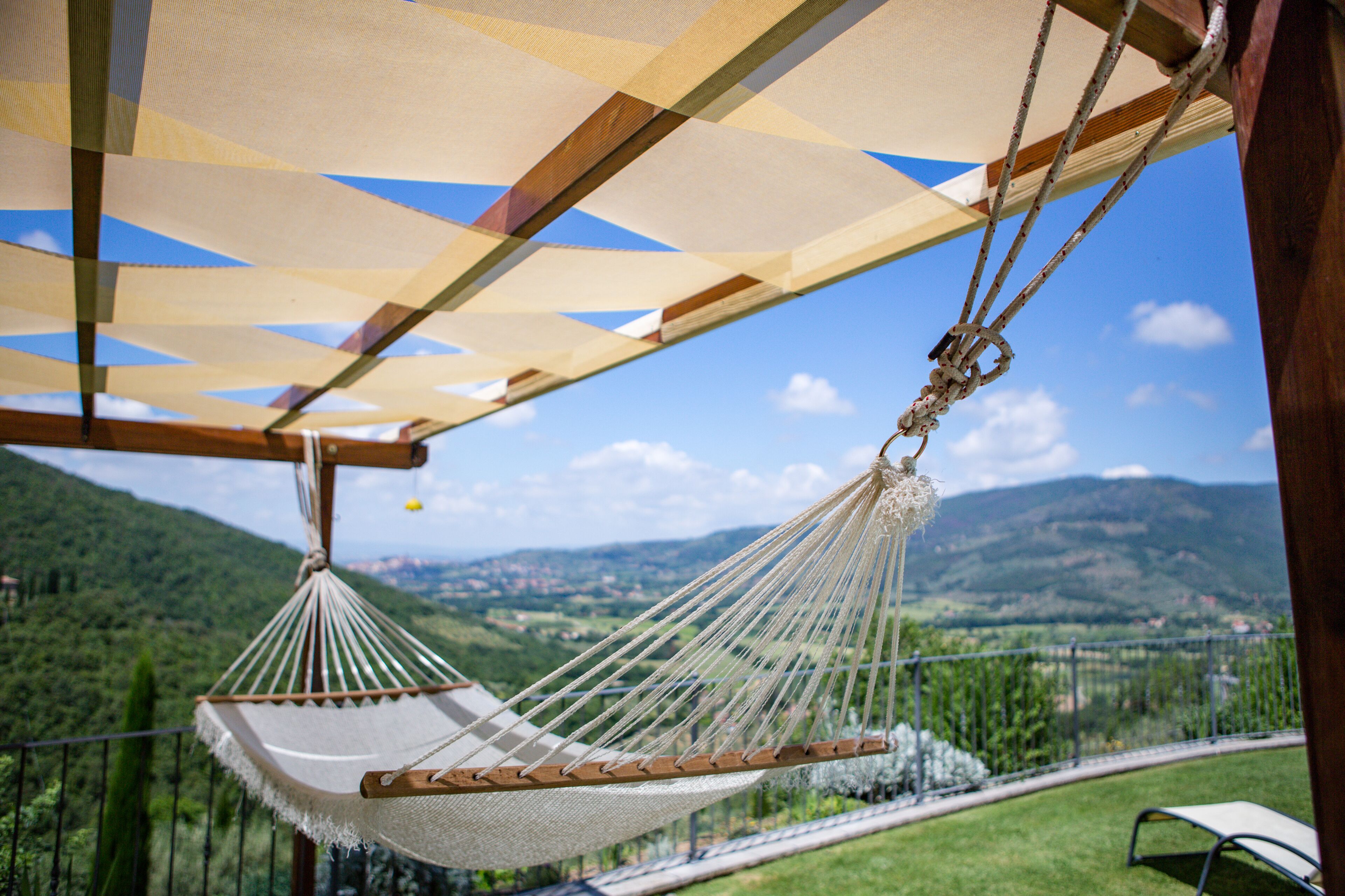 A hammock under a striped awning with a view of a mountainous landscape.