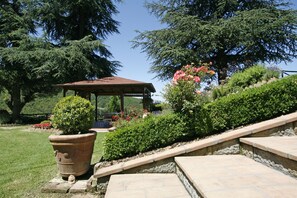 Un belvédère surmonté d’un toit en tuiles, entouré d’un jardin bien entretenu où poussent diverses plantes et fleurs.