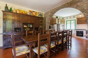 Un coin repas avec une table et des chaises en bois, un meuble contenant des objets décoratifs, et une cuisine avec un dosseret carrelé et un luminaire suspendu.