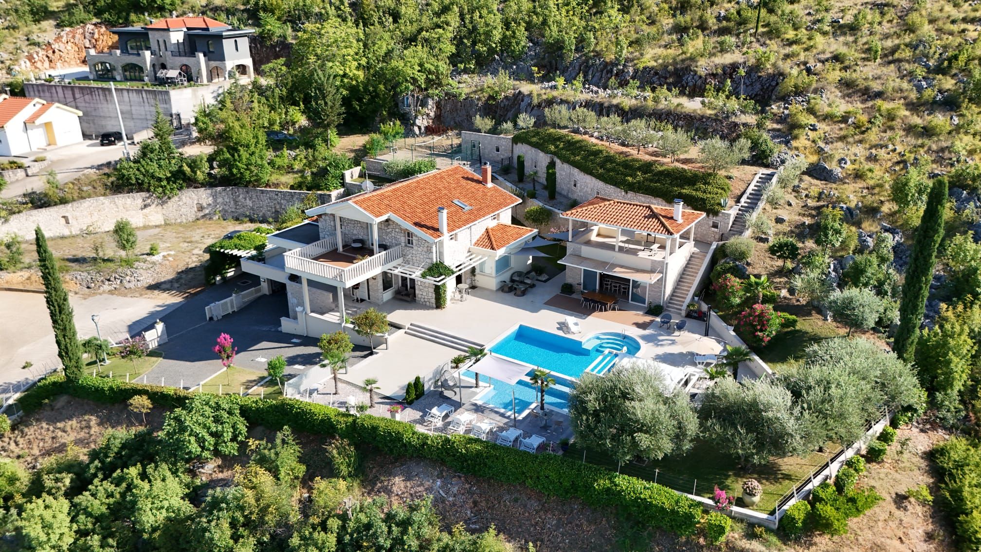 Eine großzügige, mehrstöckige Villa mit Schwimmbad, umgeben von üppiger Vegetation und einer felsigen Landschaft.
