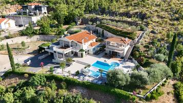 Eine großzügige, mehrstöckige Villa mit Schwimmbad, umgeben von üppiger Vegetation und einer felsigen Landschaft.