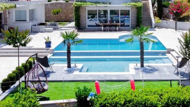 Une villa moderne dotée d’une piscine, de murs en pierre et offrant une vue sur une colline verdoyante.