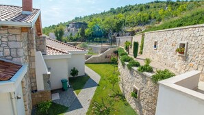 Une cour bordée de murs en pierre, surmontée d’un toit en tuiles et comprenant un espace herbeux.